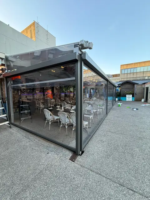 Clear PVC screens enclosing a cafe's outdoor dining area with tables set inside