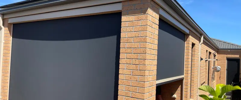 Close-up of an outdoor blind's headbox and side channel on a brick wall