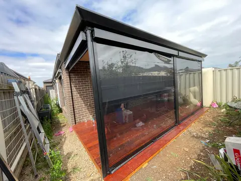 Clear PVC screens enclosing a timber pergola over a red-stained deck