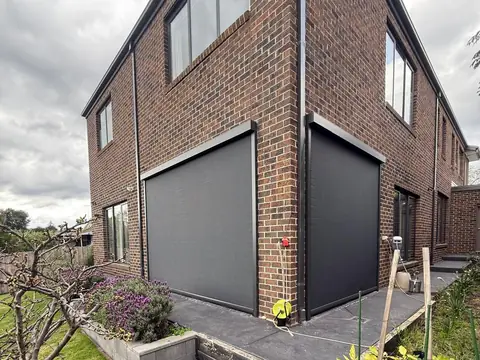 Charcoal outdoor blinds closing in the alfresco corner of a two-storey brick home