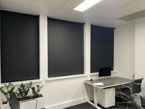 Office with dark blockout roller blinds fitted to a wall of windows